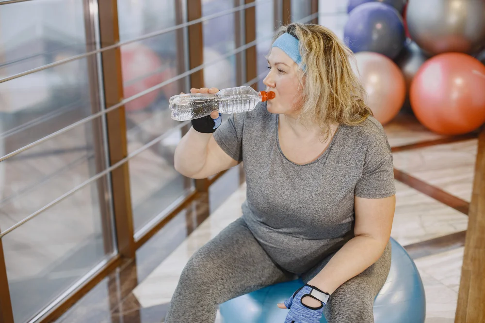 Fat woman dieting, fitness. lady sitting on a fitball and driking a water.