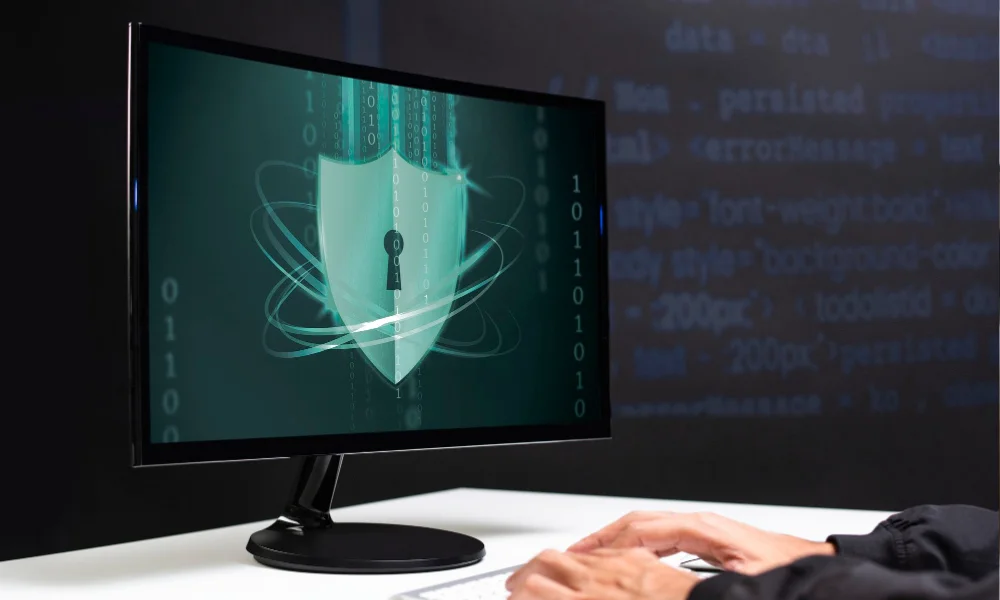 A digital shield on a monitor represents cybersecurity.