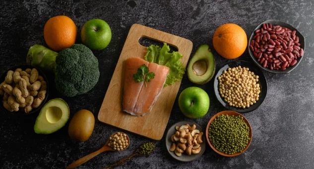 Legumes, fruit, and salmon fish pieces on a wooden chopping board.