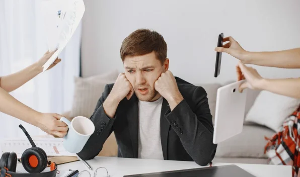 Stressed man overwhelmed by multitasking at work.