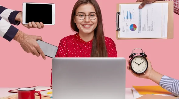 Horizontal shot of smiling beautiful woman in red shirt, sits in front of opened laptop computer