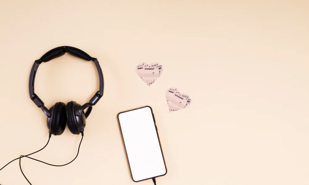 Smartphone with headphones and paper hearts with music notes on beige background.