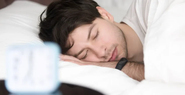 Young man sleeping next to alarm clock wearing smart wristband