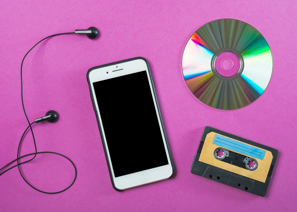 iPhone with earphones placed beside CD and cassette on pink background