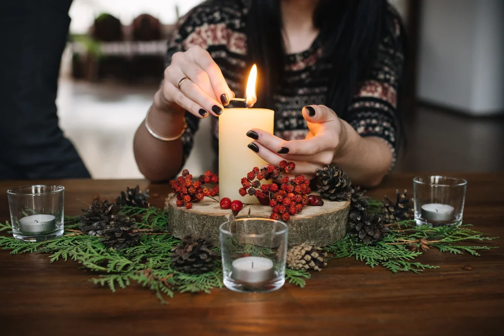 Close-up of a hand lighting a candle surrounded by fresh herbs and citrus.