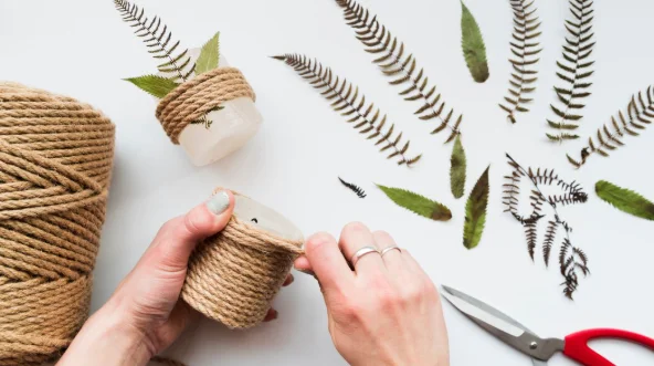 Woman's hand wrapping the string on candle with leaves and scissor-diy crafts for home decor