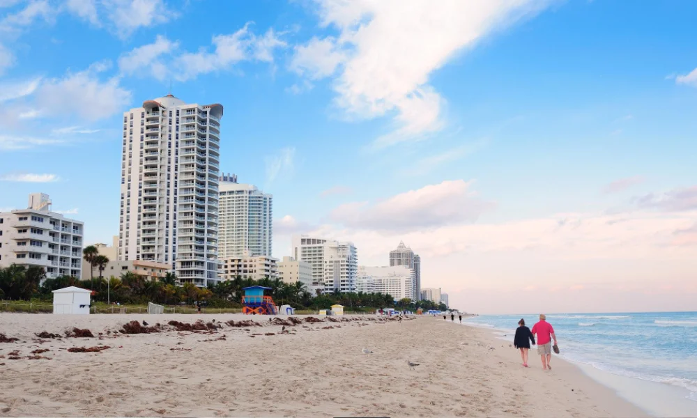People walking along a sandy beach lined with Miami high-rise condos.