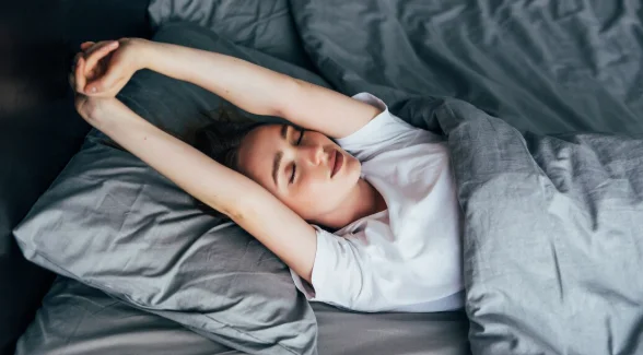 Attractive woman stretching in the morning and is smiling in her bed-lifestyle factors definition