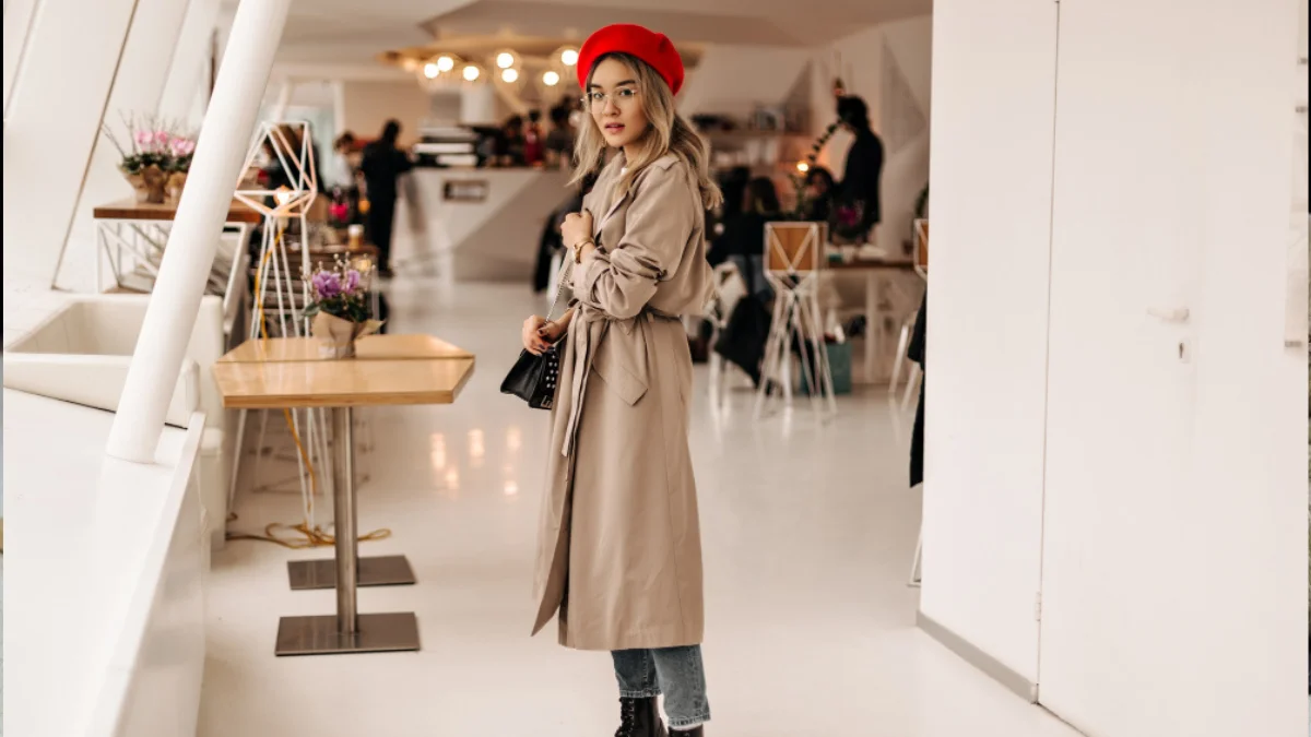 Woman in beige trench coat and red beret with black bag in cafe, embodying Quiet Luxury Brands.